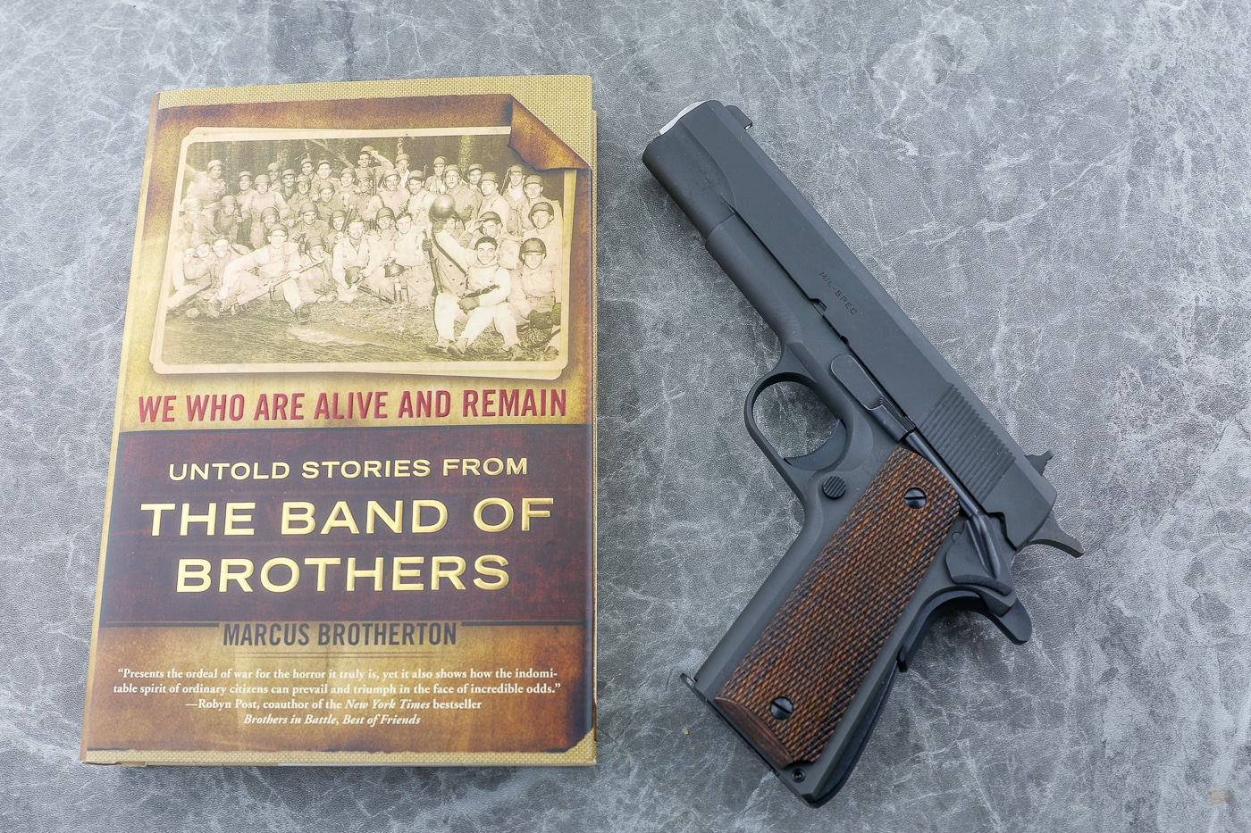 A modern 1911 pistol rests beside a copy of Band of Brothers, the historical book documenting Easy Company paratroopers during World War II. War trophy narratives fill military literature extensively. Combat veterans sought dependable sidearms desperately. Historical accounts document soldiers' firearm quests. Trophy weapons appeared throughout wartime memoirs. Military handguns provided psychological reassurance. War souvenirs connected servicemen to survival. Captured pistols symbolized battlefield advantages gained. Trophy firearms represented security under fire.