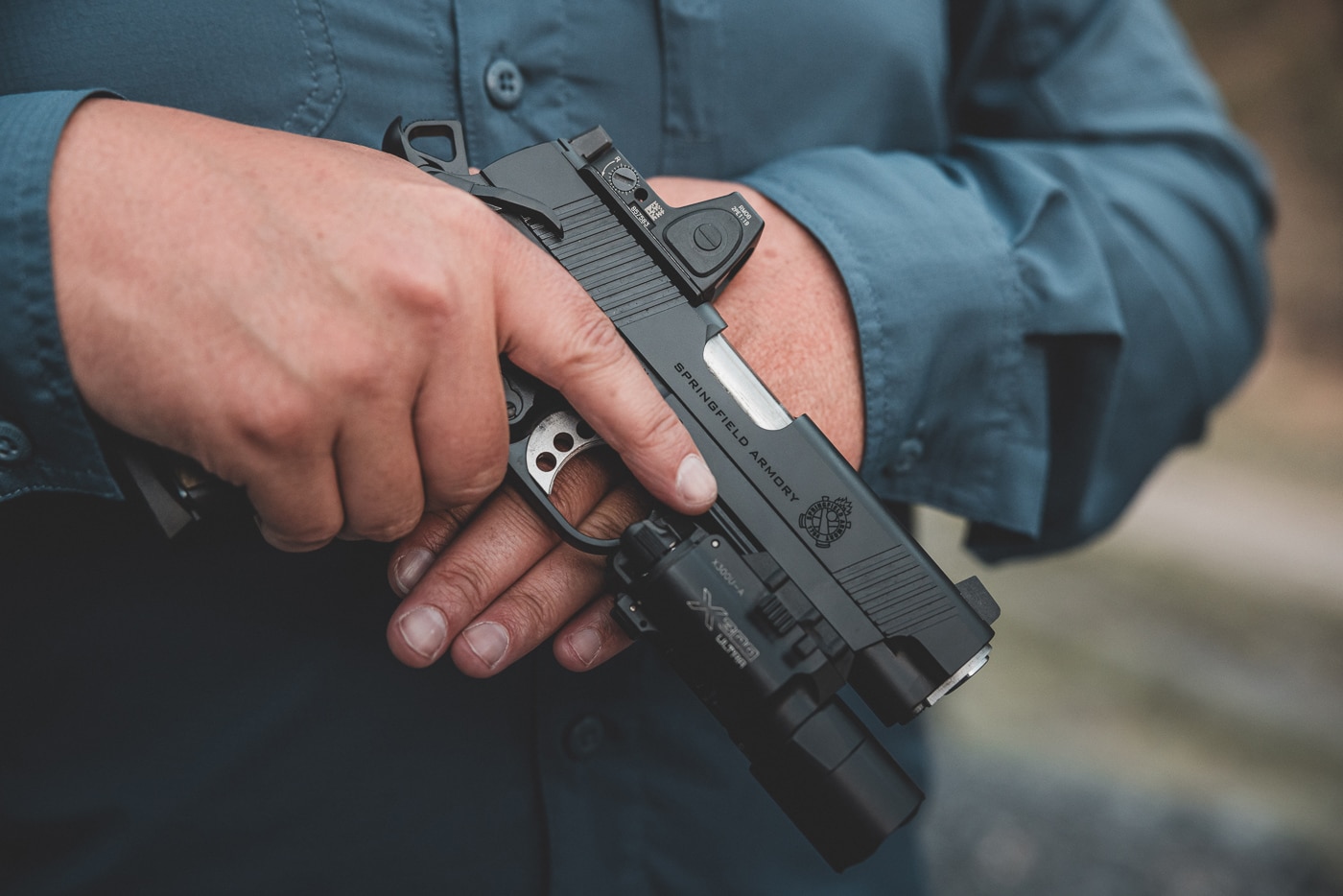 The author grips a Springfield Operator 1911 pistol demonstrating proper thumb placement on the manual safety lever. The 1911 pistol's strengths include superior trigger control characteristics. Single-action mechanisms provide consistent pull weights. Ergonomic grip angles enhance natural pointing ability. Ambidextrous safety options accommodate different shooters. The 1911 pistol's weaknesses involve size and weight considerations. Steel-frame construction increases carry mass. Slim single-stack magazines limit ammunition capacity. Quality 1911 pistols deliver exceptional shooting accuracy.