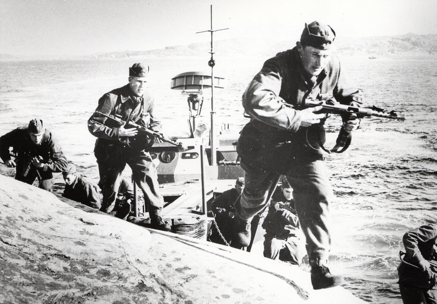 Swedish military personnel conducting an amphibious landing operation while carrying Carl Gustaf m/45 submachine guns with water splashing around them as they move from boats to shore. Open bolt firearms function in wet conditions. Closed bolt guns require careful protection. Carl Gustaf m/45 used open bolt design. Swedish submachine guns emphasized reliability. Open bolt systems resist water damage. Amphibious operations demand robust weapons. Military firearms handle extreme environments. Open bolt mechanisms maintain operational readiness.