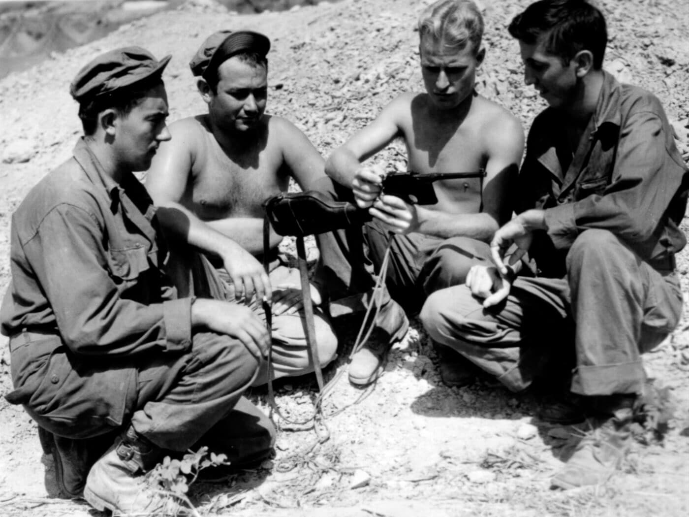 Multiple American soldiers in combat uniforms examine a captured German-made Mauser C96 broomhandle pistol found on Okinawa during the final months of World War II in the Pacific. War trophy acquisition was widespread among troops. Captured enemy sidearms generated significant interest. Battlefield firearms became highly sought mementos. Soldiers prized seized adversary weapons. Trophy pistols symbolized combat victories achieved. Confiscated armaments represented defeated opponents. War souvenirs validated dangerous missions survived. Military keepsakes held profound psychological value.