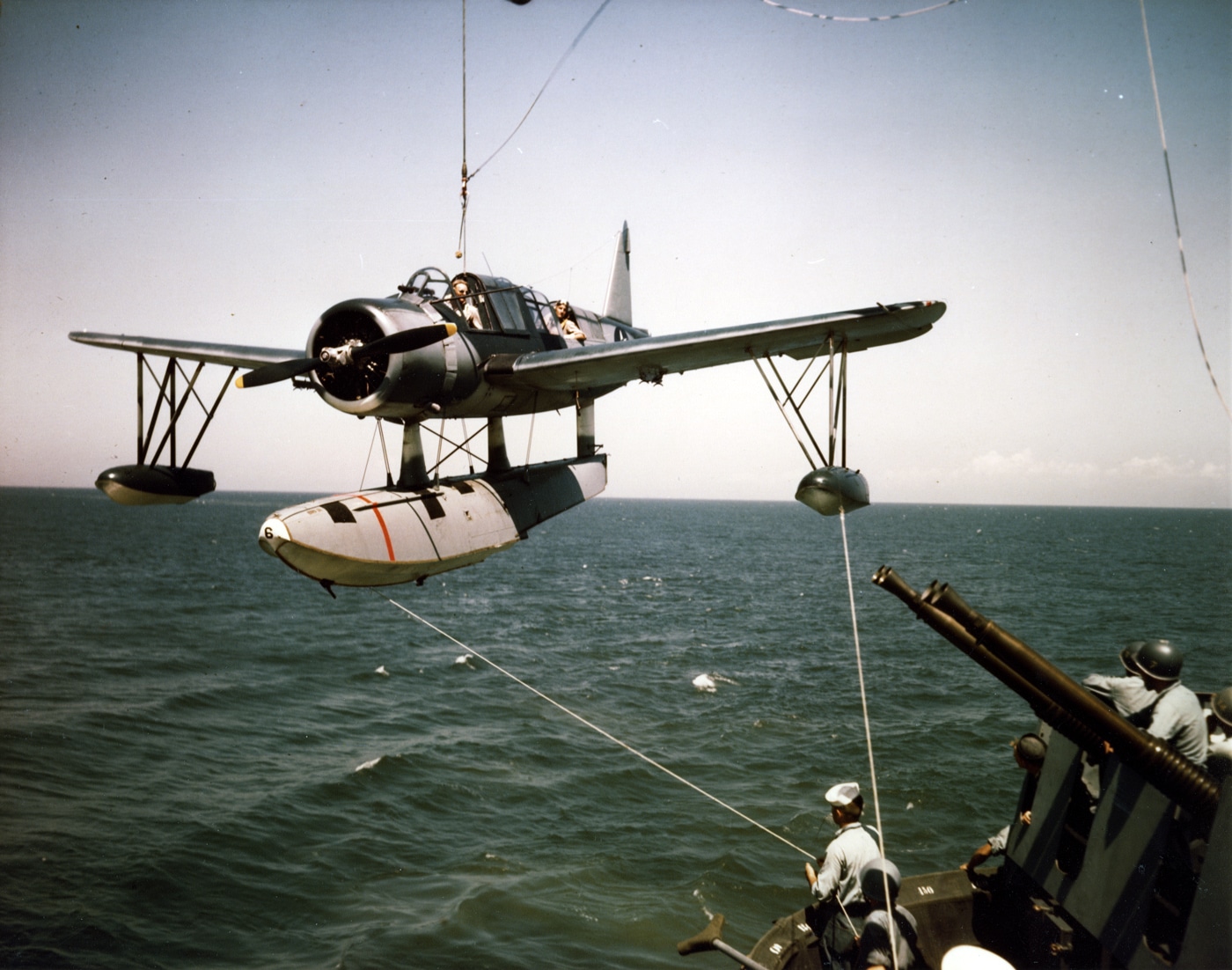 A Vought OS2U Kingfisher floatplane is being lifted by crane onto the deck of the USS Missouri battleship, with its distinctive floats visible beneath the fuselage and crew members visible on deck coordinating the recovery operation. The Vought OS2U Kingfisher served American battleships. Kingfisher floatplanes provided aerial reconnaissance capabilities. Naval observation aircraft spotted gunfire during combat operations. Shipboard catapults launched reconnaissance floatplanes. OS2U aircraft featured all-metal monoplane construction. Kingfisher floatplane crews rescued downed aviators. Battleship-based spotter planes improved gunnery accuracy. Vought-manufactured observation aircraft operated throughout the Pacific.