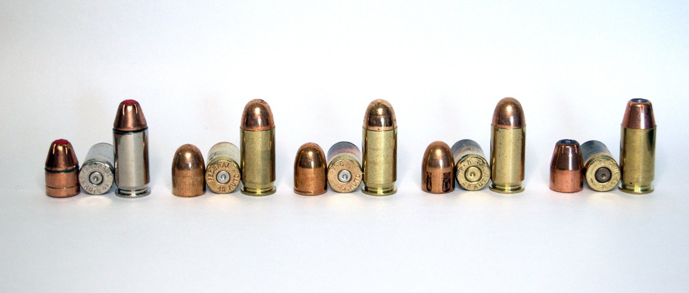 An assortment of .45 ACP ammunition including Federal, Hornady, and PMC brands arranged on a surface showing different bullet types from FMJ to hollow points. M1911 pistols function with diverse ammunition as woods guns. Springfield Armory Garrison cycles various M1911 cartridge types. The .45 ACP offers extensive loading options. FMJ bullets provide deep penetration. Hollow point rounds deliver controlled expansion. Woods gun ammunition requires reliability testing. Premium defensive loads suit specific threats. Multiple bullet weights accommodate different scenarios.