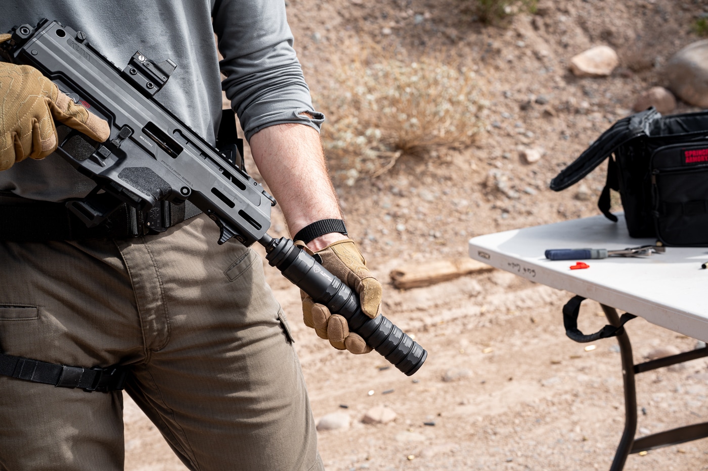 A photograph showing the author's hands threading the JK Armament 155 RPX 9mm suppressor onto the muzzle of a Springfield Armory Kuna pistol caliber carbine. The JK Armament suppressor review demonstrated easy installation. Taper mounts provide secure suppressor attachment. The RPX 9mm silencer aligns properly on threaded barrels. Shooters value quick-attach systems for convenience. The Kuna accepts standard muzzle devices readily. Proper mounting ensures reliable suppressor function. The modular design allows fast configuration changes. Sound suppressors should seat firmly before firing.