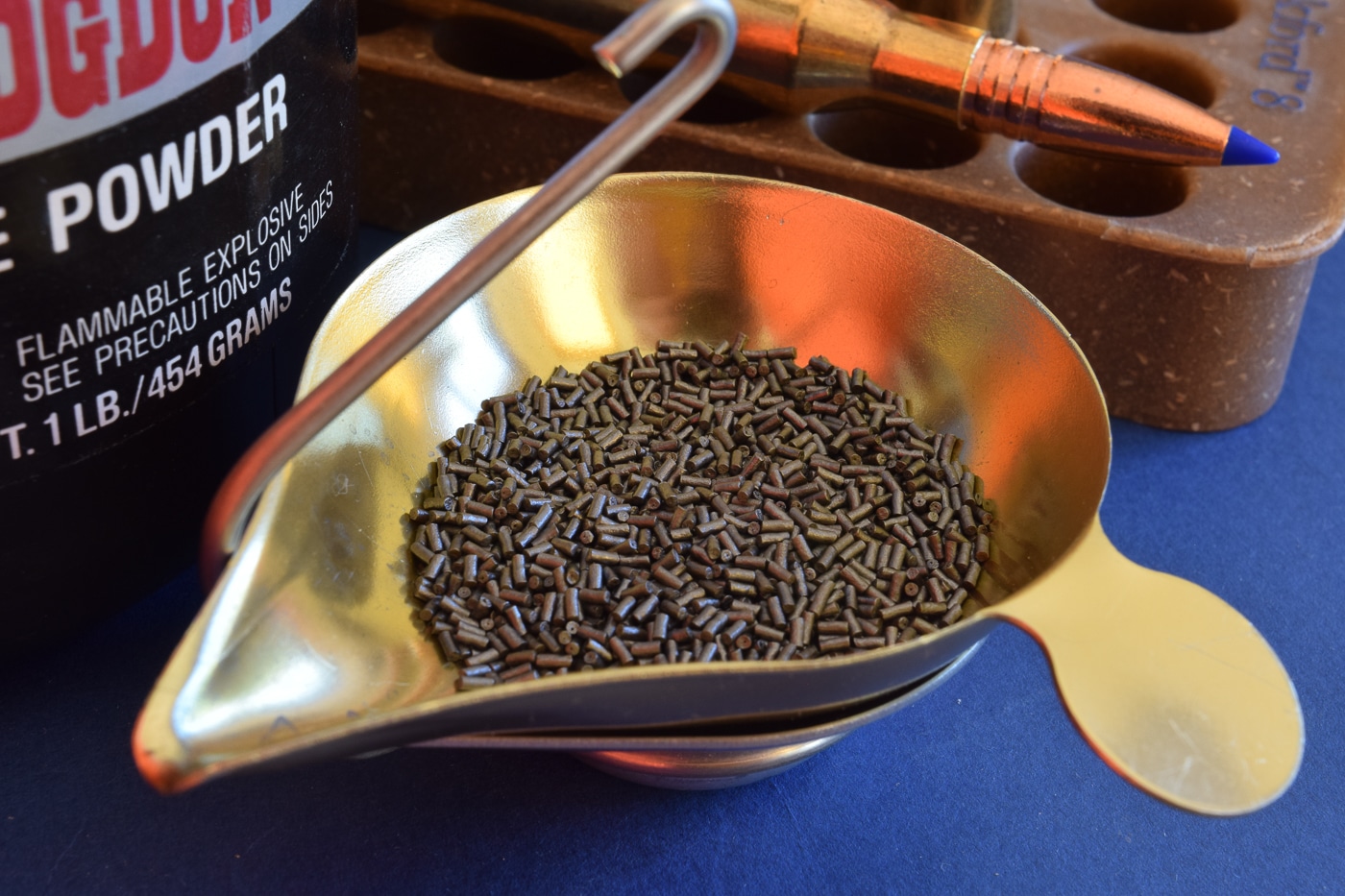 A close-up photograph shows gray cylindrical extruded gunpowder grains scattered on a surface, each stick-shaped granule featuring a hollow tubular structure that burns progressively from both internal and external surfaces simultaneously. Gunpowder history includes grain geometry innovations. Extruded powders burn progressively during combustion. Origins of gunpowder refinement involved structural designs. IMR series uses extruded stick formulations. Progressive burning extends thrust duration. Gunpowder origins evolved beyond simple grain shapes. DuPont developed extruded powder technology. Ancient propellants lacked sophisticated engineering.