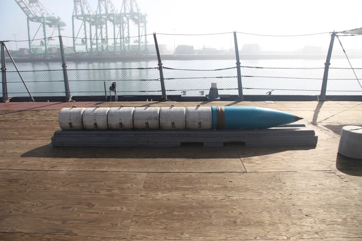 A photograph shows a large 16-inch practice artillery shell positioned at the breech opening of a naval gun, demonstrating the loading process used on battleships. Mark 23 nuclear shells required careful breech loading procedures. Project Katie training utilized practice projectiles extensively. Naval gun crews loaded rounds weighing nearly one ton. The Mark 7 gun system fired various shell types. Battleship turrets employed 79-man operating crews. Practice ammunition prepared gunners for nuclear round handling. Each ship maintained nine training shells onboard. Loading drill rounds certified gunner crew proficiency.