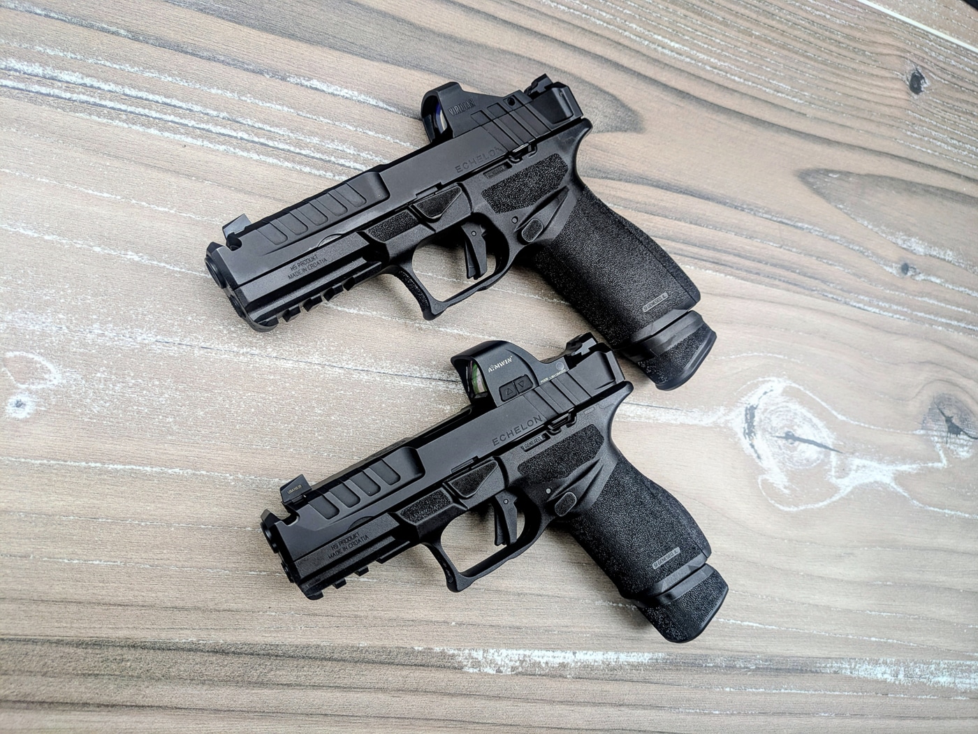 Two black Springfield Armory Echelon pistols displayed side by side on a neutral surface, showing the full-size 4.5F Comp model and the compact 4.0C Comp model with their integral compensator ports visible on the slides. Compensated Echelon comparison demonstrates performance differences between sizes. Springfield Echelon 4.0C Comp vs Echelon 4.5F Comp highlights barrel length variations. Striker-fired handguns feature modular frame systems. Polymer-frame pistols include ambidextrous controls throughout. Integral compensators reduce felt recoil effectively. Variable Interface System mounts optics directly. Adaptive Grip Texture enhances shooter comfort. Magazine capacity options accommodate different applications.