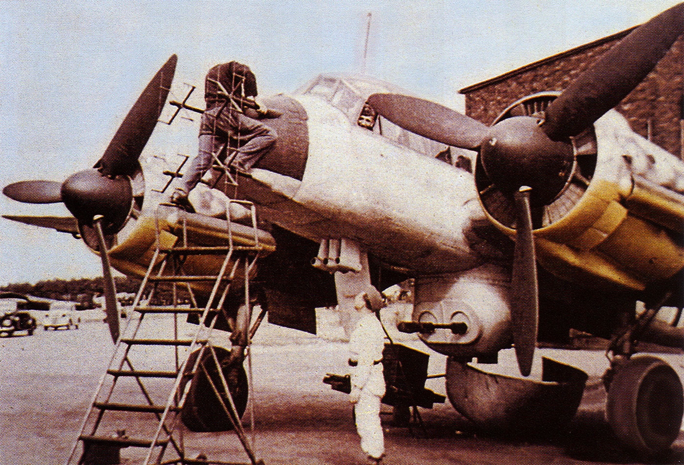 Ground crew technicians installing a FI-A-103Z gun pack onto a Junkers Ju 88G night fighter aircraft during maintenance operations. The Ju 88 bomber evolved into capable night fighter variants. German night fighters defended against Allied bombing raids. Gun pack installations increased offensive firepower significantly. Luftwaffe ground crews maintained complex weapon systems. Ju 88G models featured enhanced armament configurations. Night fighter operations required specialized equipment modifications. Upward-firing cannons attacked bomber undersides effectively. Technical improvements continued throughout production runs.