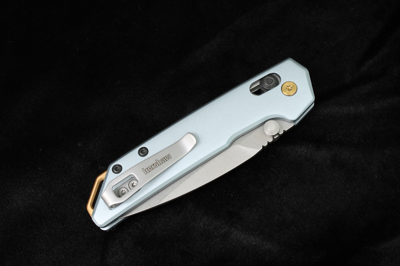 The photograph shows a Kershaw Mini Iridium folding knife featuring an ice blue anodized aluminum body with gold accent details, creating a distinctive gentleman's knife aesthetic with modern styling. Kershaw knives offer unique color options. Anodized aluminum provides durable finishes. Affordable knives escape tactical monotony. The Mini Iridium features crossbar locking. Gentleman's folders suit refined tastes. Kershaw models incorporate ball bearing pivots. Ice blue anodization creates premium appearance. Affordable knives deliver upscale aesthetics. Gold accents enhance visual appeal.