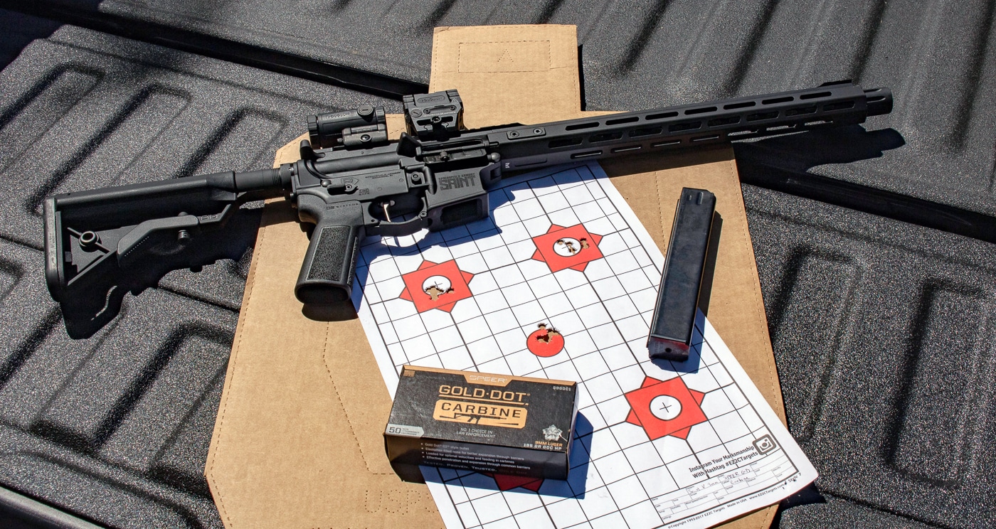 A Springfield Armory SAINT Victor 9mm carbine rests on a shooting bench alongside boxes of Speer Gold Dot Carbine ammunition and testing equipment. Speer Gold Dot Carbine ammunition underwent comprehensive range testing. PCC ammo evaluation included accuracy and velocity measurements. The SAINT Victor features AR-pattern ergonomics. Gold Dot loads come in nickel-plated brass cases. Pistol caliber carbines offer improved shootability over handguns. The Speer Gold Dot Carbine review tested multiple performance metrics. Carbine ammunition requires proper evaluation protocols. Springfield Armory SAINT Victor accepts 32-round magazines.