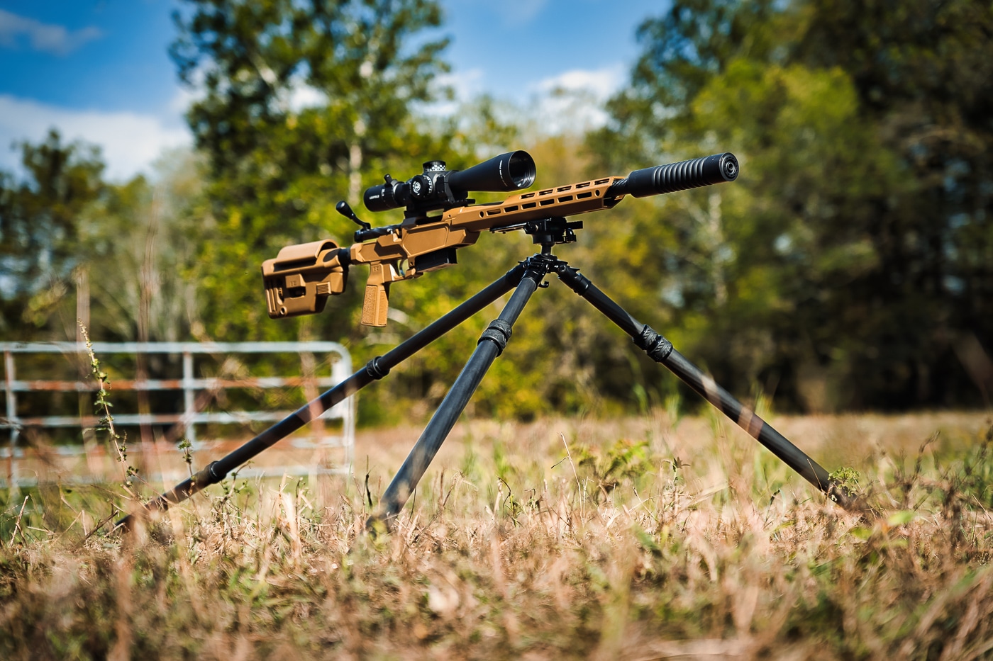 A Springfield Armory Model 2020 Heatseeker rifle with scope is mounted on a Tricer-HK tripod via Arca-Swiss plate in an outdoor setting. The Tricer-HK tripod review showcases rifle compatibility features. Ultra light Tricer-HK tripod evaluation confirms .308 Winchester support capability. Arca-Swiss mounting enables quick rifle attachment.