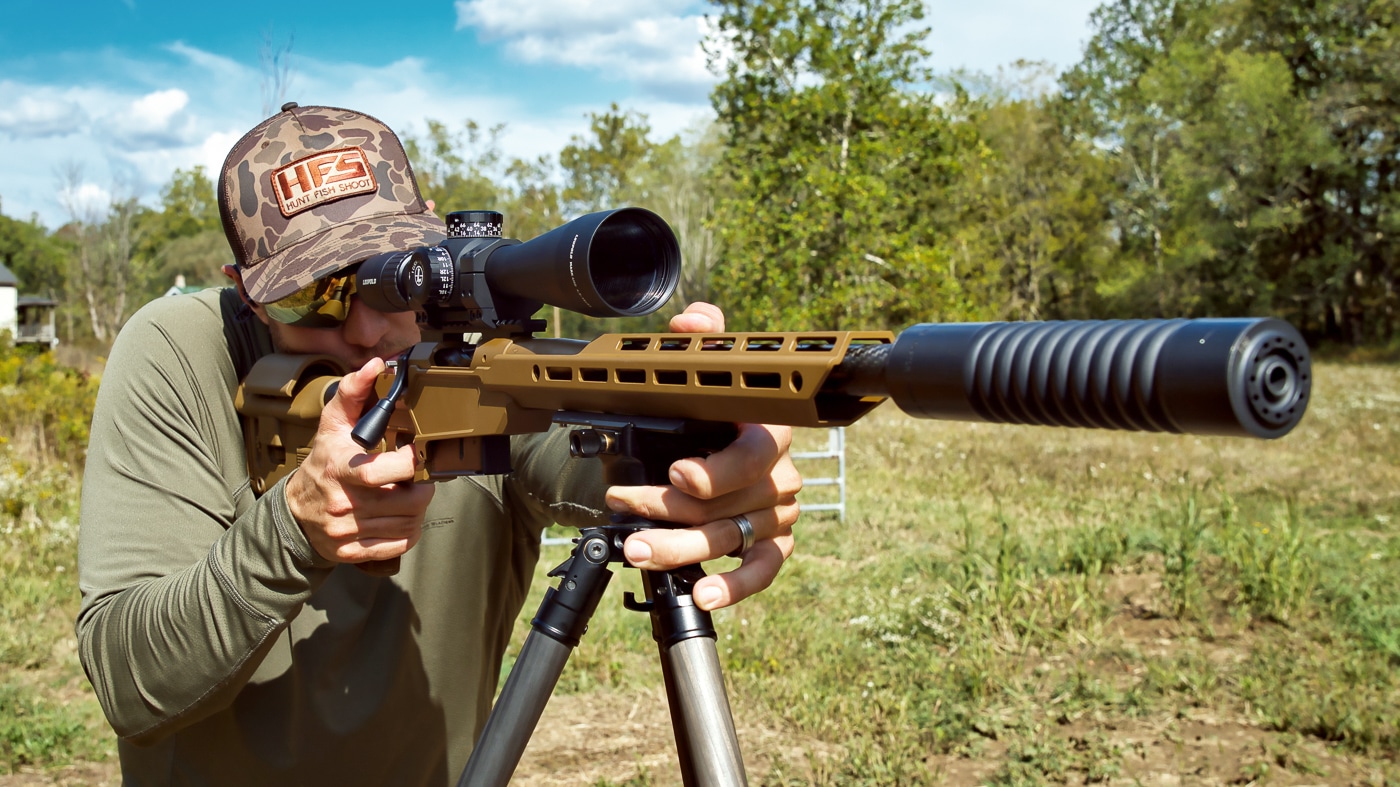 A carbon fiber Tricer-HK tripod with AK ball head mounted rifle system displayed against a neutral background, showing the inverted leg design and Arca-Swiss compatible mounting system. The Tricer-HK tripod review demonstrates exceptional weight-to-stability ratios. Ultra light Tricer-HK tripod evaluation reveals superior backcountry performance. Precision shooting platforms benefit from carbon fiber construction.