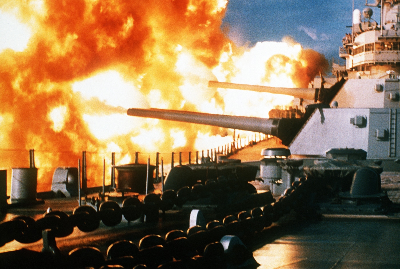 A powerful photograph captures the USS New Jersey battleship firing a salvo from its massive 16-inch Mark 7 guns off the coast of Beirut, Lebanon on January 9, 1984, with enormous muzzle flashes and smoke erupting from multiple gun barrels simultaneously. Mark 7 guns previously fired Mark 23 nuclear shells. Project Katie armed New Jersey with atomic projectiles. USS New Jersey received 1982 modernization upgrades. Battleships carried both conventional and nuclear weapons. Iowa-class vessels deployed serious firepower capabilities. Mark 160 Fire Control systems guided gun operations. New Jersey carried 32 Tomahawk cruise missiles. Naval gunfire supported Lebanon operations effectively.