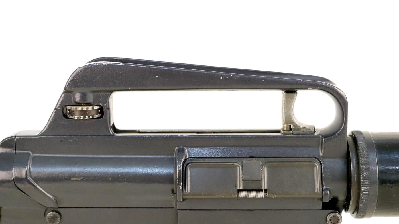 A close-up photograph of the unique charging handle mechanism on a Dutch AR-10 rifle, showing the trigger-like appendage located inside the carry handle that operates differently from modern AR designs. The AR-10 featured innovative controls. Early charging handles differed significantly. Stoner experimented with configurations. AR10 history includes design evolution. The handle provided forward assist. Dutch models used original design. Non-reciprocating operation reduced snags. Later versions changed locations.