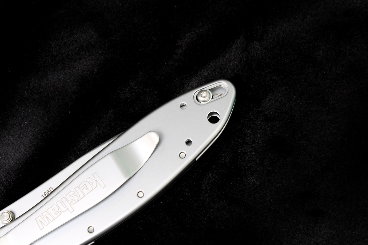 The photograph shows a close-up view of the manual safety lock mechanism located on the spine of a Kershaw Leek folding knife near the rear of the handle. Kershaw knives incorporate thoughtful safety features. Manual locks prevent unintended blade deployment. Affordable knives include multiple safety mechanisms. Assisted-opening folders require failsafe designs. The Leek combines speed with security. Kershaw models suit everyday carry scenarios. Spine-mounted switches add minimal bulk. Affordable knives balance convenience with safety. Pocket knives need reliable engagement prevention.