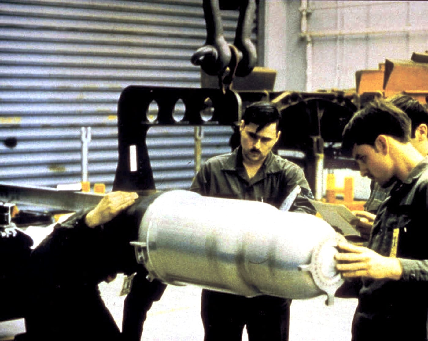 A photograph shows military technicians in protective gear carefully handling or inspecting a W80 nuclear warhead, demonstrating the precision and safety protocols required when working with atomic weapons. W80 warheads armed Tomahawk cruise missiles. Project Katie preceded TLAM-N nuclear systems. Naval nuclear weapons evolved from shells to missiles. The W80 produced 200-kiloton explosive yields. Battleships carried 32 Tomahawk missiles total. Nuclear warhead handling required Marine Corps security. TLAM-N missiles replaced Mark 23 artillery shells. Cruise missile warheads offered extended strike ranges.