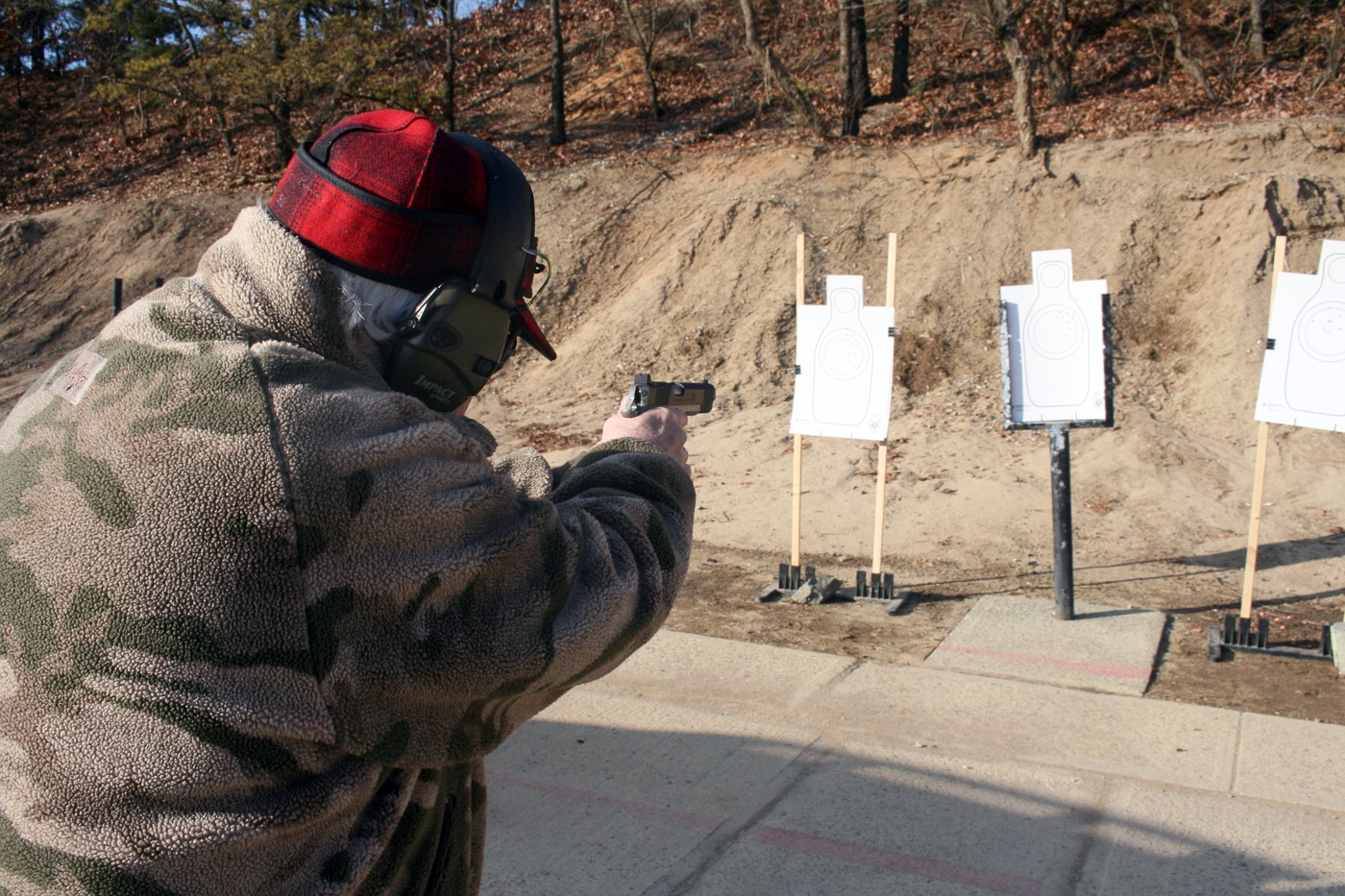 A firearms instructor demonstrates proper shooting technique while engaging multiple targets during a timed training exercise. Experienced shooters exhibit efficient transitions. Proper form maintains shooting velocity. Instructor demonstrations show correct technique. Multi-target engagement requires disciplined execution. Combat shooting fundamentals enable speed.