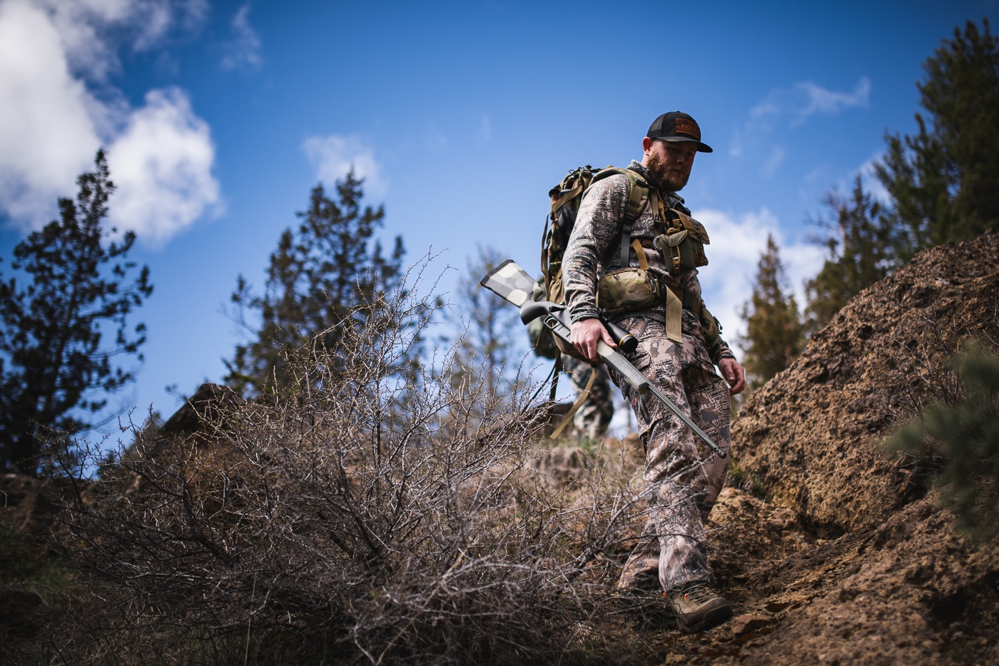 A hunter dressed in outdoor gear holds a Springfield Waypoint bolt-action rifle while standing in a forest setting during hunting season. First hunting rifle purchases require informed decisions. Beginner's hunting rifle features should match intended game. Springfield Armory rifles offer multiple cartridge options. Lightweight rifles reduce hunter fatigue. Proper ammunition selection ensures ethical harvests. 