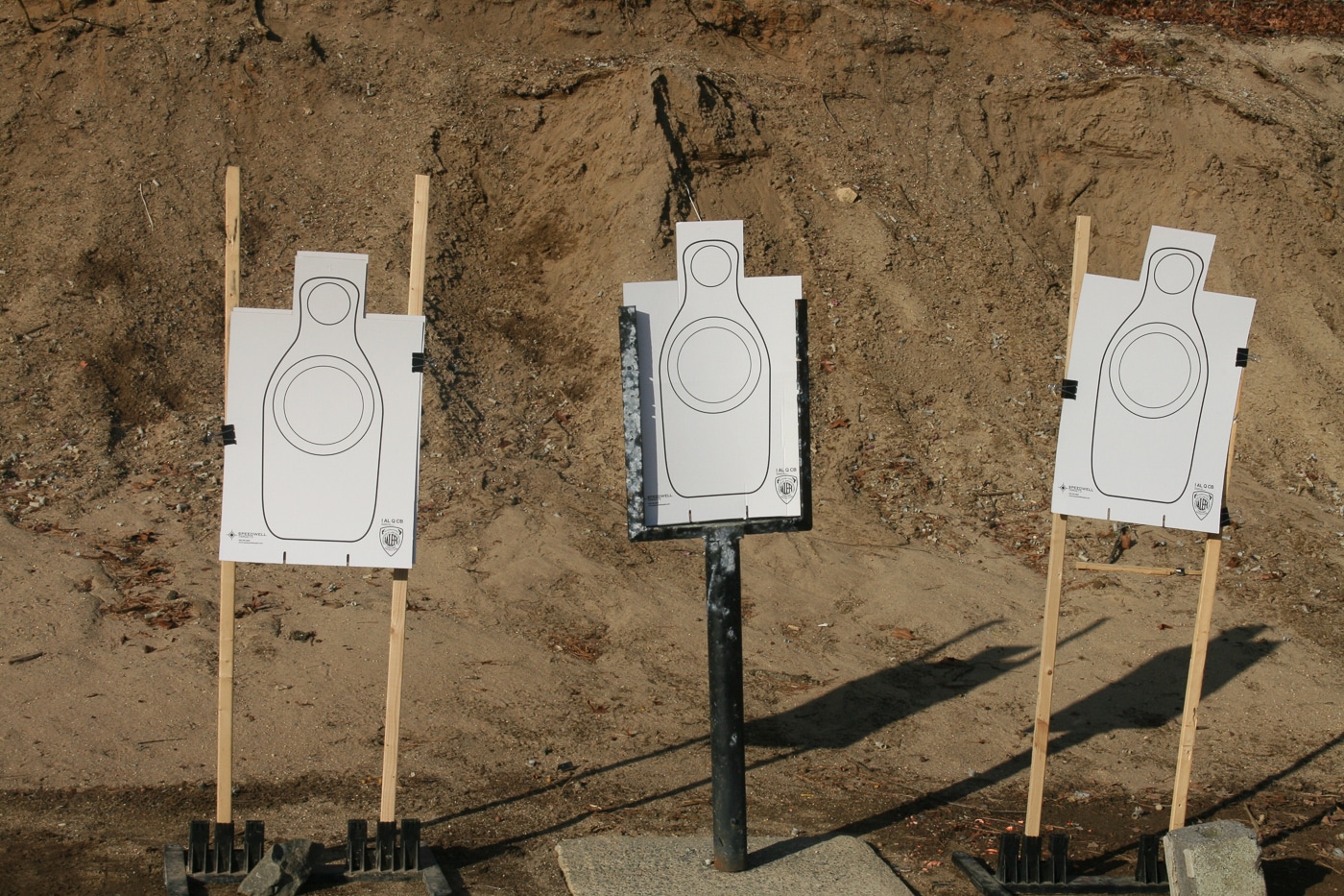 Multiple paper silhouette targets are arranged in a row with spacing between them for transition shooting practice. Target transition drills improve engagement speed. Multiple threat training enhances tactical capability. Sequential shooting exercises build proficiency. Eye movement coordination accelerates transitions. High-value zone placement demands precision. Combat scenarios involve multiple adversaries.