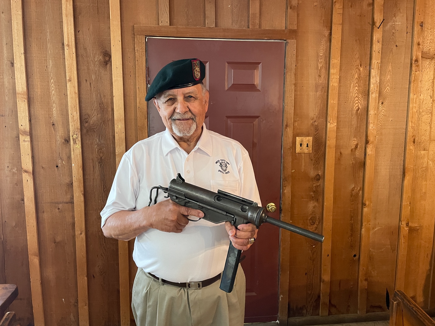 A smiling elderly man, a former Green Beret veteran, holds an M3 Grease Gun submachine gun indoors at a private residence. The AK-47 in Vietnam War history is inseparable from the American advisors who first encountered it. Special Forces soldiers carried weapons like the M3 Grease Gun before the M16 reached forward operating camps. Kalashnikov rifles captured in Vietnam were often taken from Viet Cong fighters during ambushes. U.S. Army advisors worked alongside indigenous Montagnard tribesmen in early combat operations. Vietnam War small arms included surplus WWII weapons still in active field use by American and allied forces. The Viet Cong relied on AK-47 rifles supplied by the Soviet Union and Communist China. Green Berets serving in Vietnam frequently encountered Chinese Type 56 Kalashnikov variants. Early AK-47 rifles captured in Vietnam were considered rare and strategically significant trophies.