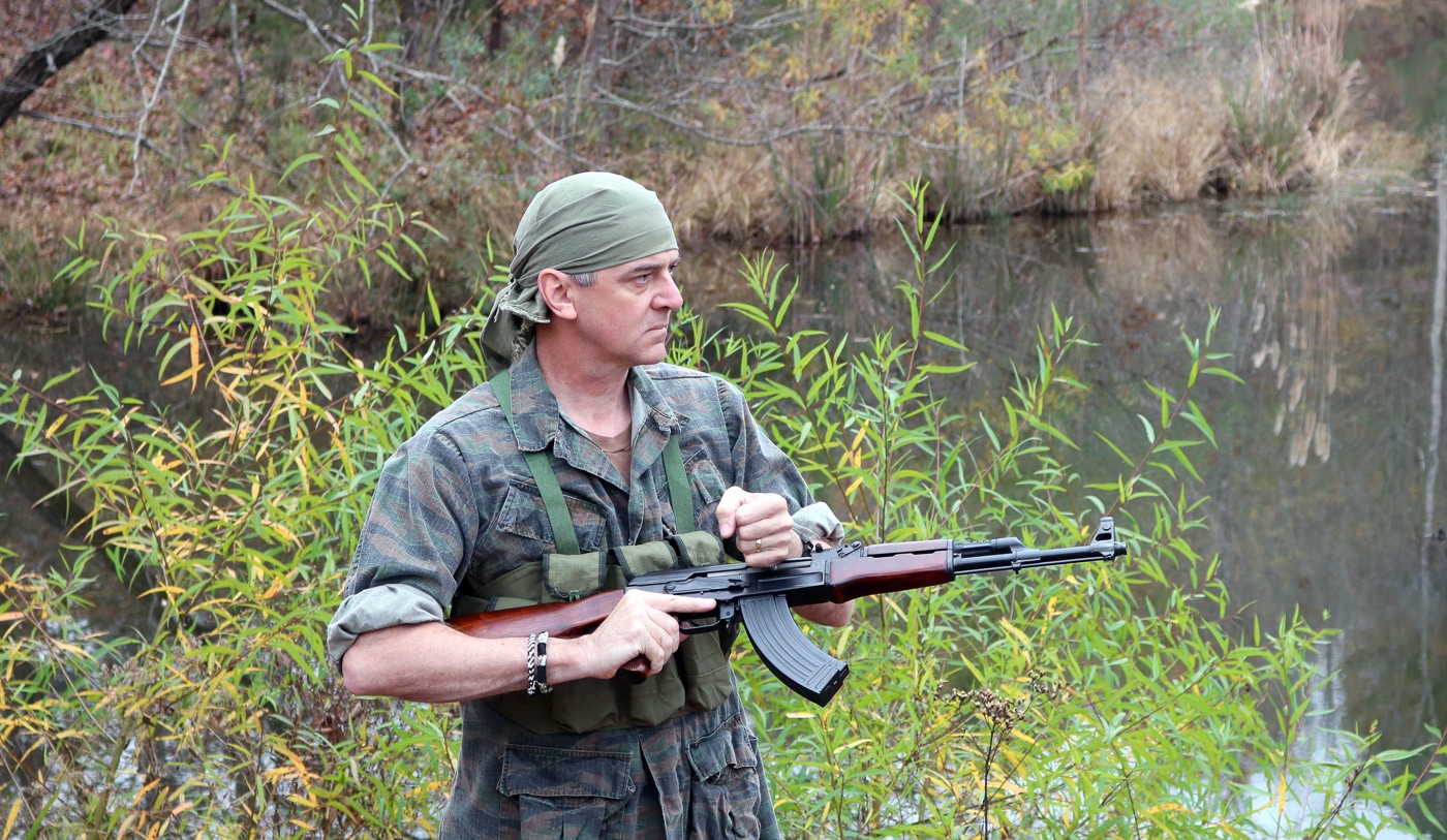 A man charges the bolt of an AK-47 assault rifle while standing outdoors in a field setting. The AK-47 in Vietnam War combat was renowned for its straightforward operation under the most demanding conditions. Kalashnikov rifles were deliberately designed for simplicity so that minimally trained fighters could operate them effectively. Viet Cong guerrillas used AK-47 rifles to ambush American patrols in dense jungle terrain throughout the war. The charging handle of the AK-47 is located on the right side of the receiver for intuitive one-handed operation. Vietnam War infantry tactics frequently involved close-quarters engagements where the AK-47's maneuverability was a decisive advantage. U.S. Special Forces soldiers occasionally used captured Kalashnikov rifles during covert operations in Southeast Asia.
