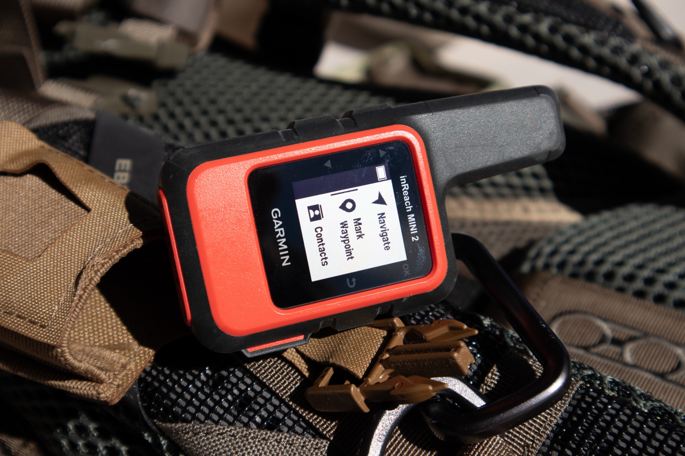 A close-up view of the Garmin inReach Mini 2 satellite communicator clipped to a piece of outdoor equipment, with its display visible and a textured grip designed for harsh conditions. Off-grid survival communication tools save backcountry lives. Satellite devices transmit beyond cell towers. Hunters depend on inReach units. Emergency messaging contacts staffed dispatchers. The best off-grid communication gear withstands rough handling. Lightweight builds reduce pack weight. Two-way texts share precise locations. Preparedness mindsets favor proven technology.
