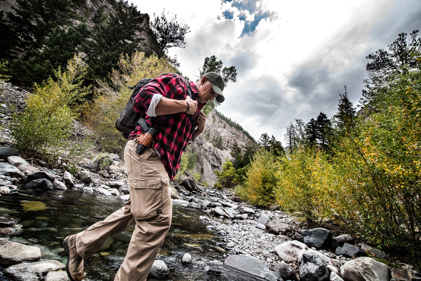 man hiking with Springfield XD-M Elite 10mm pistol and crossing a creek