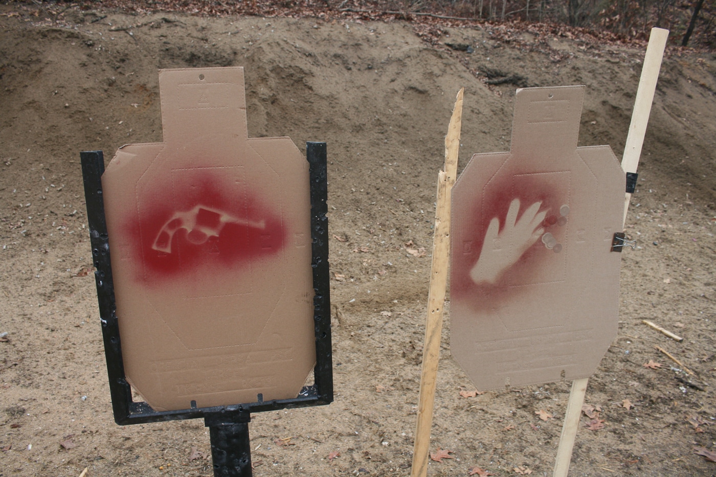 Several brown cardboard silhouette targets stand on a range with spray-painted images on their chests, some showing weapons and others showing empty hands or harmless objects. Using stenciled designators turns a basic shooting drill into a genuine evaluation exercise for the concealed carrier. The shooter has to process visual information and confirm a deadly danger before deciding to engage. This approach mirrors the real-world challenge of separating an aggressor from an innocent bystander in a chaotic scene. Ability, opportunity, jeopardy, and preclusion all become relevant once the target is revealed. Building judgmental elements into static range work is one of the most accessible ways to sharpen defensive decision-making.