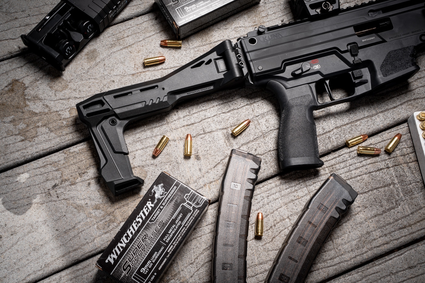 The photograph shows the Springfield Armory Kuna, a compact PDW-style 9mm pistol, fitted with the Strike Industries Polymer FSA STAB folding brace mounted to its rear Picatinny rail. This image opens my Strike Industries Kuna STAB review at The Armory Life. The STAB, short for stabilizer, is a direct Picatinny-mounted folding stabilizing brace built for PDW-style pistols. Strike Industries molds it from fiber-reinforced Polymer Extreme material to keep weight near 12 ounces without giving up rigidity. On the Kuna platform, the brace preserves the pistol's balance while adding a useful point of contact for recoil control. Its slim contours visually blend with the receiver, which is one reason the pairing looks so natural.