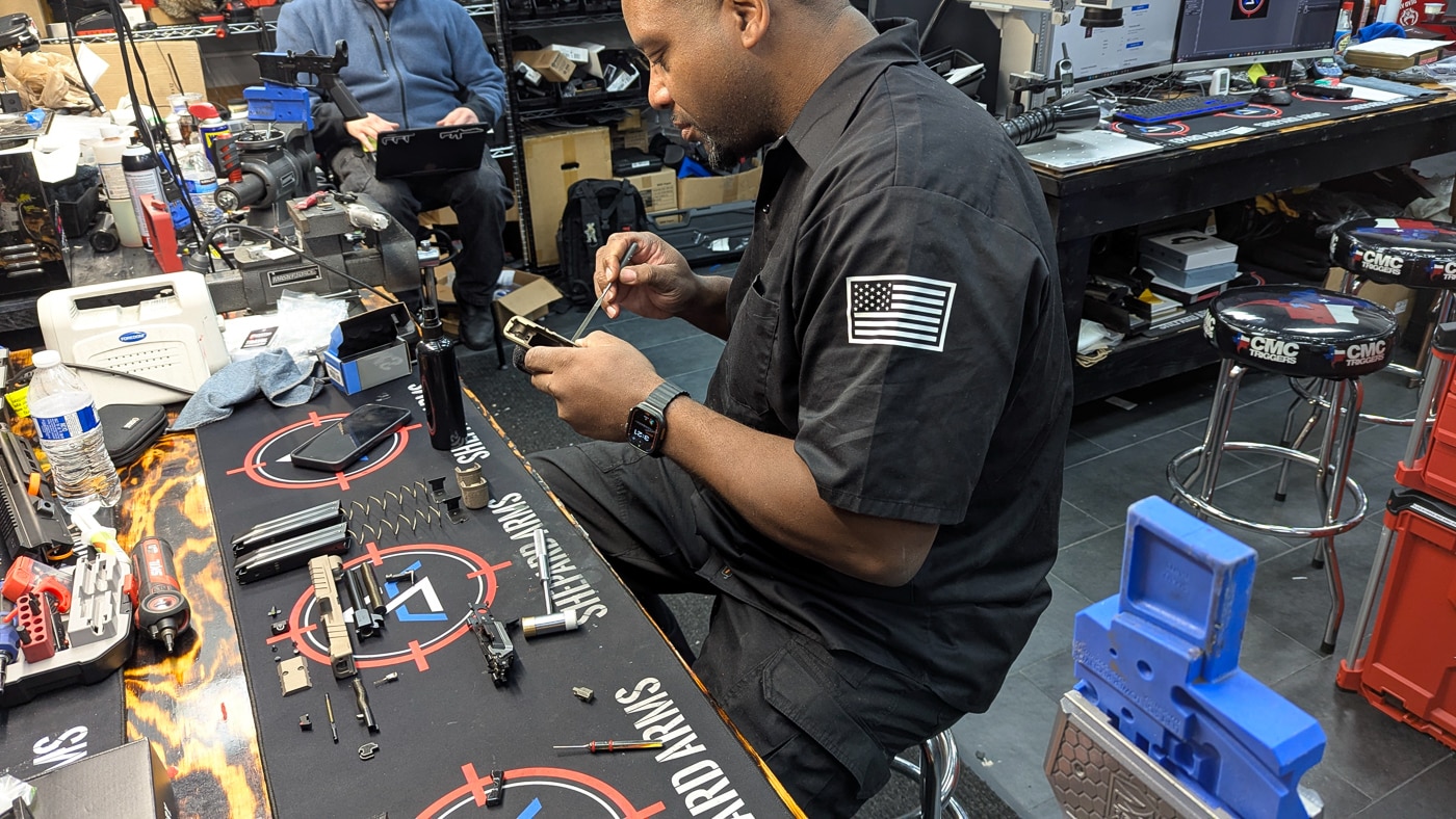Dameian Shepard, owner of Shepard Arms in Menomonee Falls, Wisconsin, carefully inspects the fit of the controls on a freshly finished Springfield Armory Echelon grip module at his gunsmithing workbench. This Shepard Arms Custom Shop Echelon review highlights how the shop's owner takes a direct role in quality control, personally verifying that every component meets his standards before a build is completed. The Echelon's interchangeable grip module system makes it one of the most accessible striker-fired platforms for custom work, allowing gunsmiths to finish and reassemble components without compromising the serialized Central Operating Group chassis. Proper control fit is a critical step in any custom pistol build, ensuring that the magazine release, slide stop and trigger function exactly as intended after finishing work like Cerakote application. Shepard Arms has built its reputation on combining technical precision with genuine craftsmanship, a standard that starts at the workbench and carries through to the finished product. The shop specializes in Cerakote finishes, laser engraving and complete custom builds, offering services that rival larger operations. Attention to detail at every stage of the process is what makes the difference between a pistol that looks custom and one that actually is.