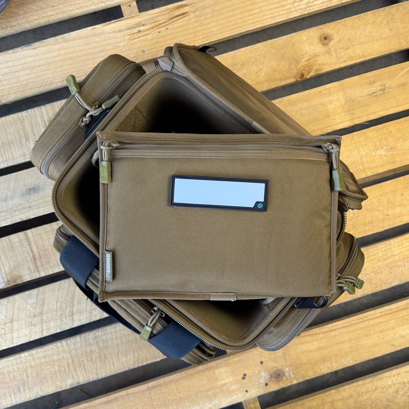 A photo captures the Savior Specialist Range Bag during range testing, standing upright with its rigid frame supporting the loaded interior. The Specialist earned its place as a go-to shooting bag through hard use both indoors and outdoors. Its organization system was clearly designed by people who understand what a range trip actually involves. The removable center divider lets the gear bag accommodate larger items when needed, while write-on ID patches help identify contents at a glance.