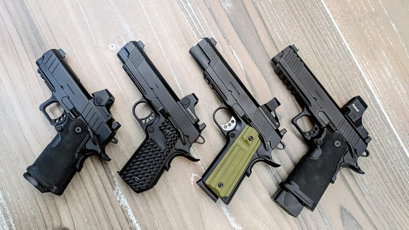 A collection of Springfield Armory 1911 and Prodigy handguns rests on a surface, each pistol topped with a different red dot sight. These 1911 optics let shooters place a single illuminated reticle on the target rather than aligning front and rear iron sights. The reflex sights shown here represent several of the most popular pistol optic footprints on the market.
