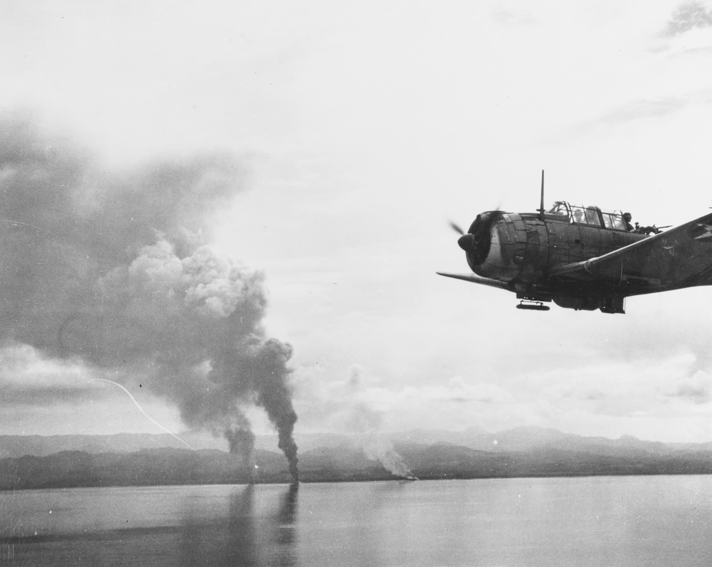 Japanese transports burn while SBD Dauntless dive bombers fly by