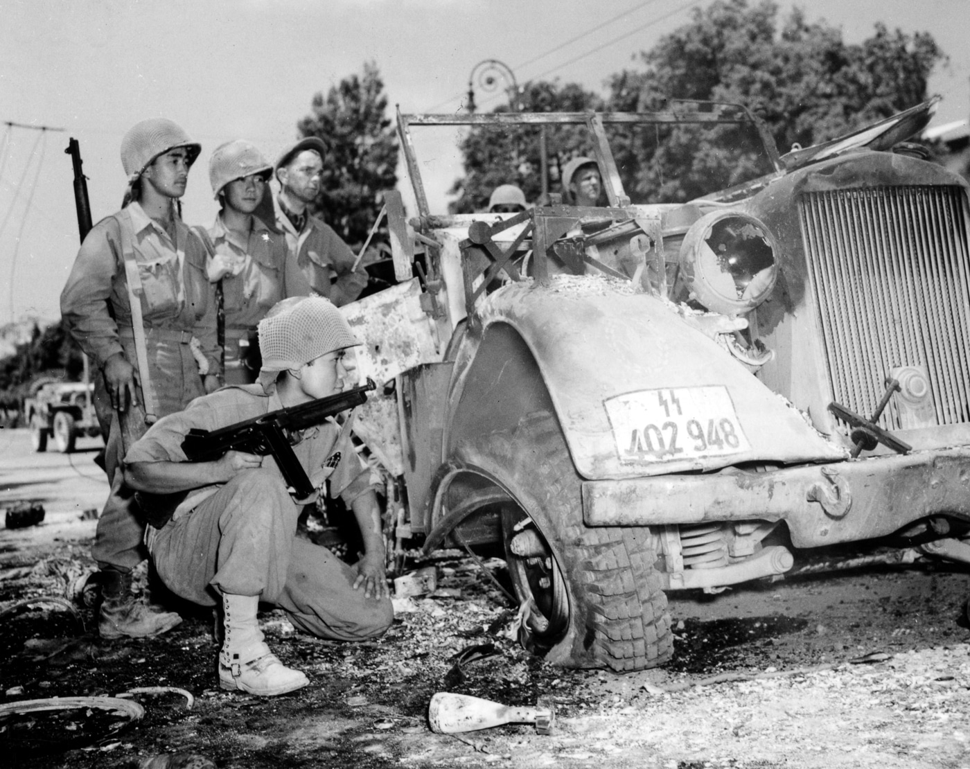 US soldier with Thompson submachine gun examines destroyed German vehicle July 1944