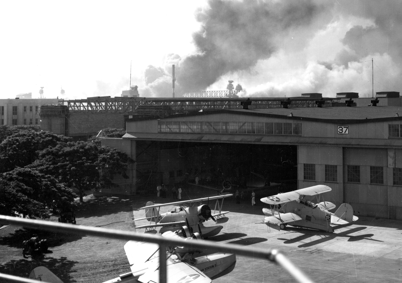 two J2F Duck planes visible outside hangar at Ford Island NAS during Pearl Harbor attack