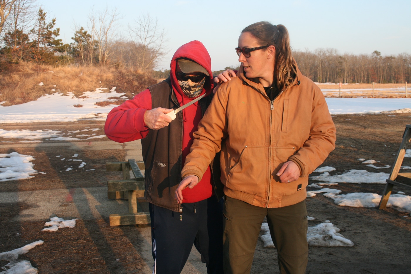 woman in winter conditions on uneven ground attacked from behind by a man with a knife