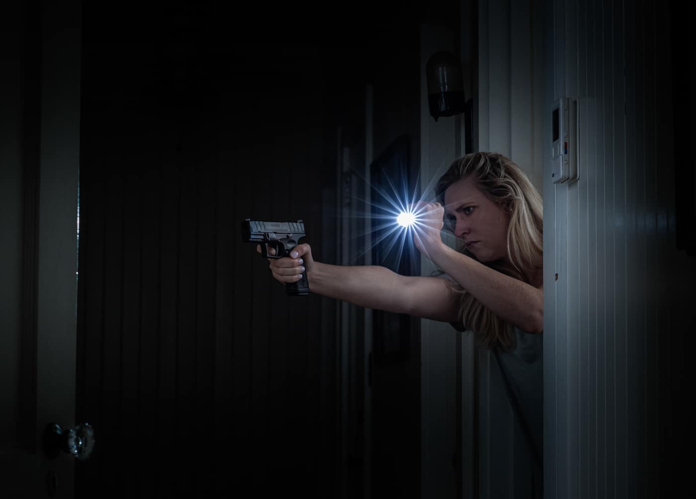 a woman with a Springfield Armory pistol uses a flashlight to illuminate a threat during a home defense scenario